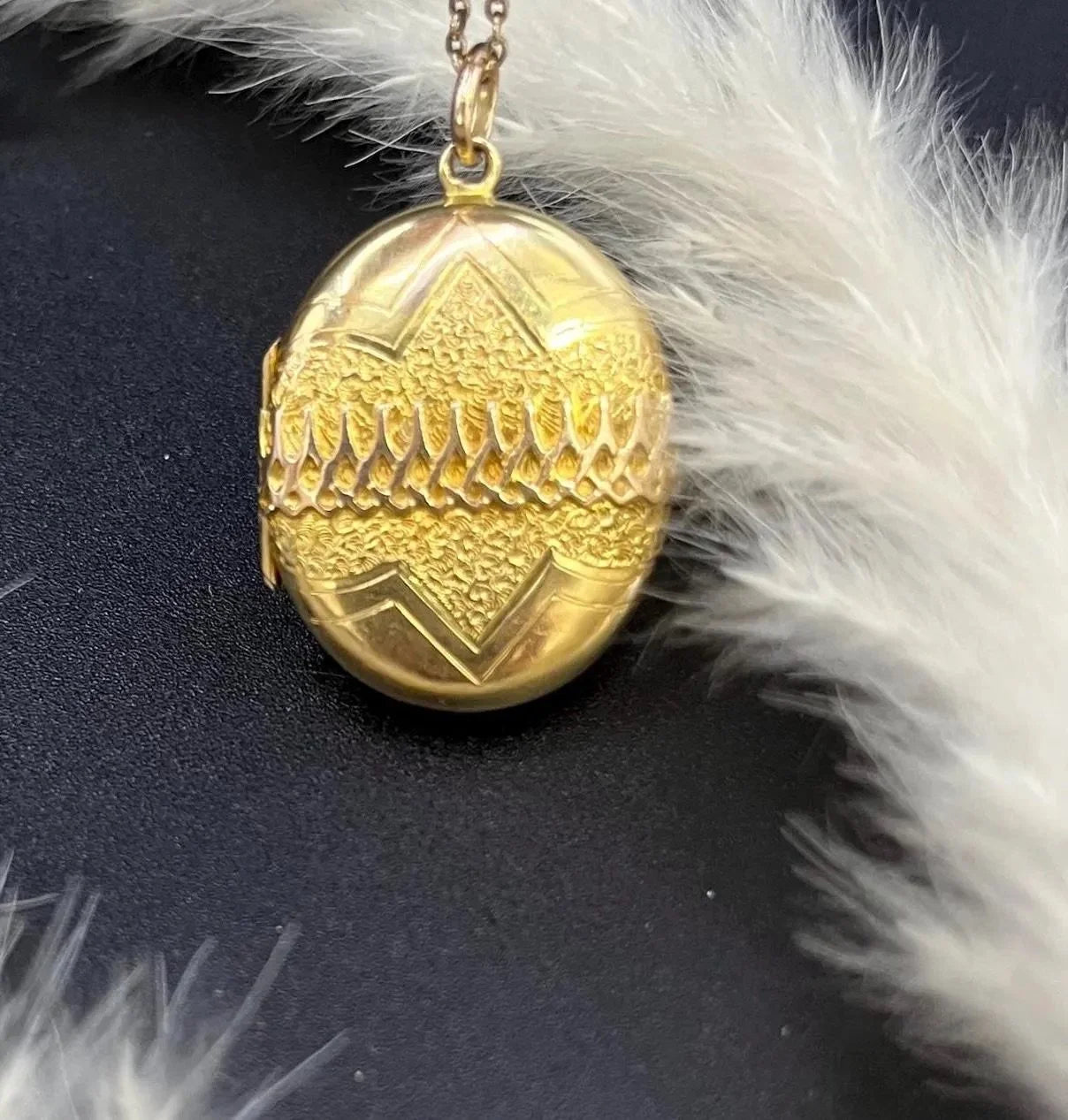 A yellow gold oval patterned locket pendant, with a chain