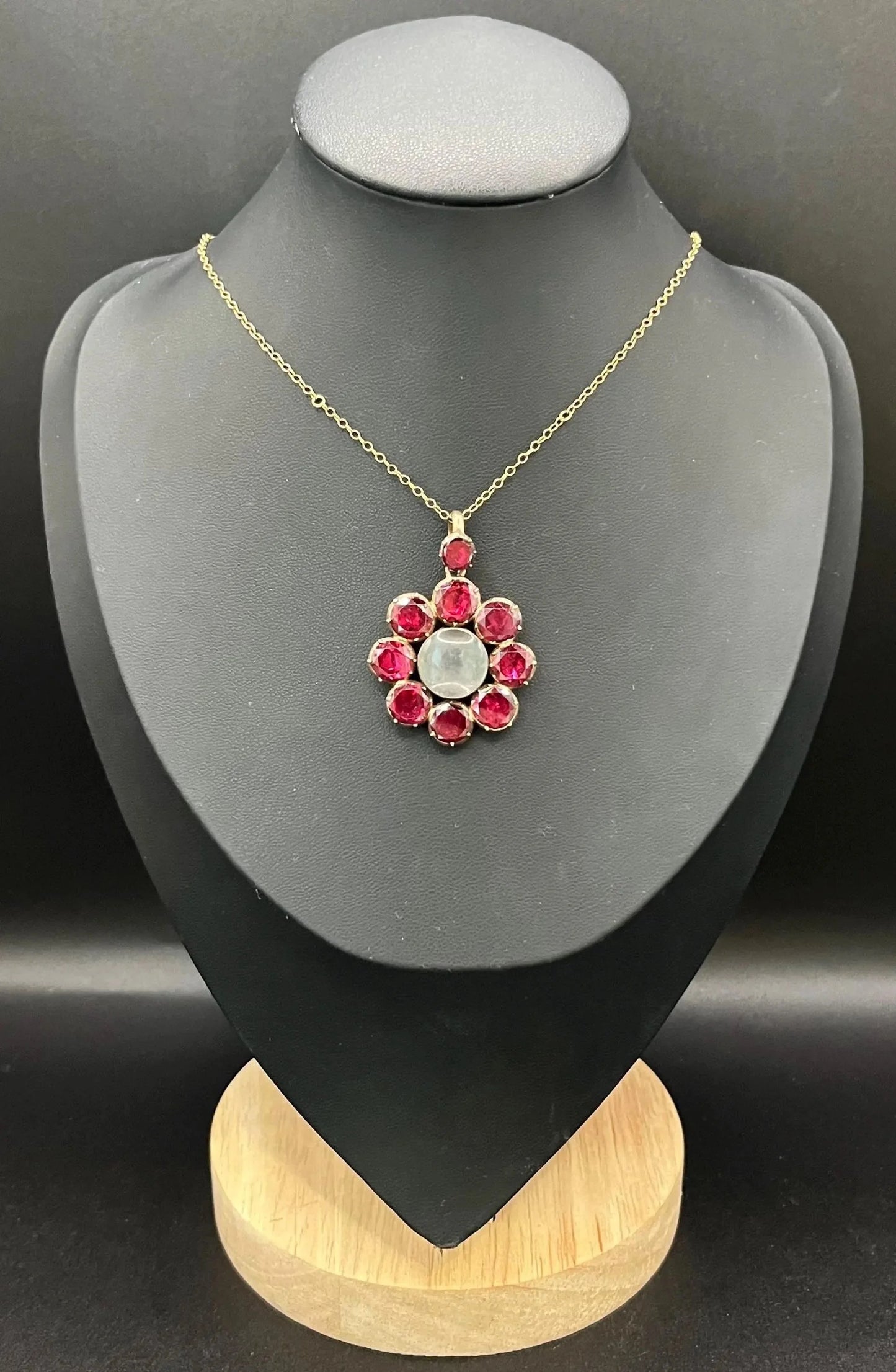 An antique garnet locket pendant in gold, with a chain, on a black bust