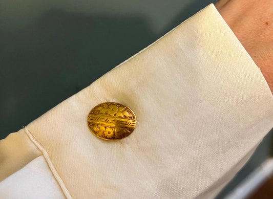 An oval yellow gold floral engraved cufflink, modelled in a white shirt cuff