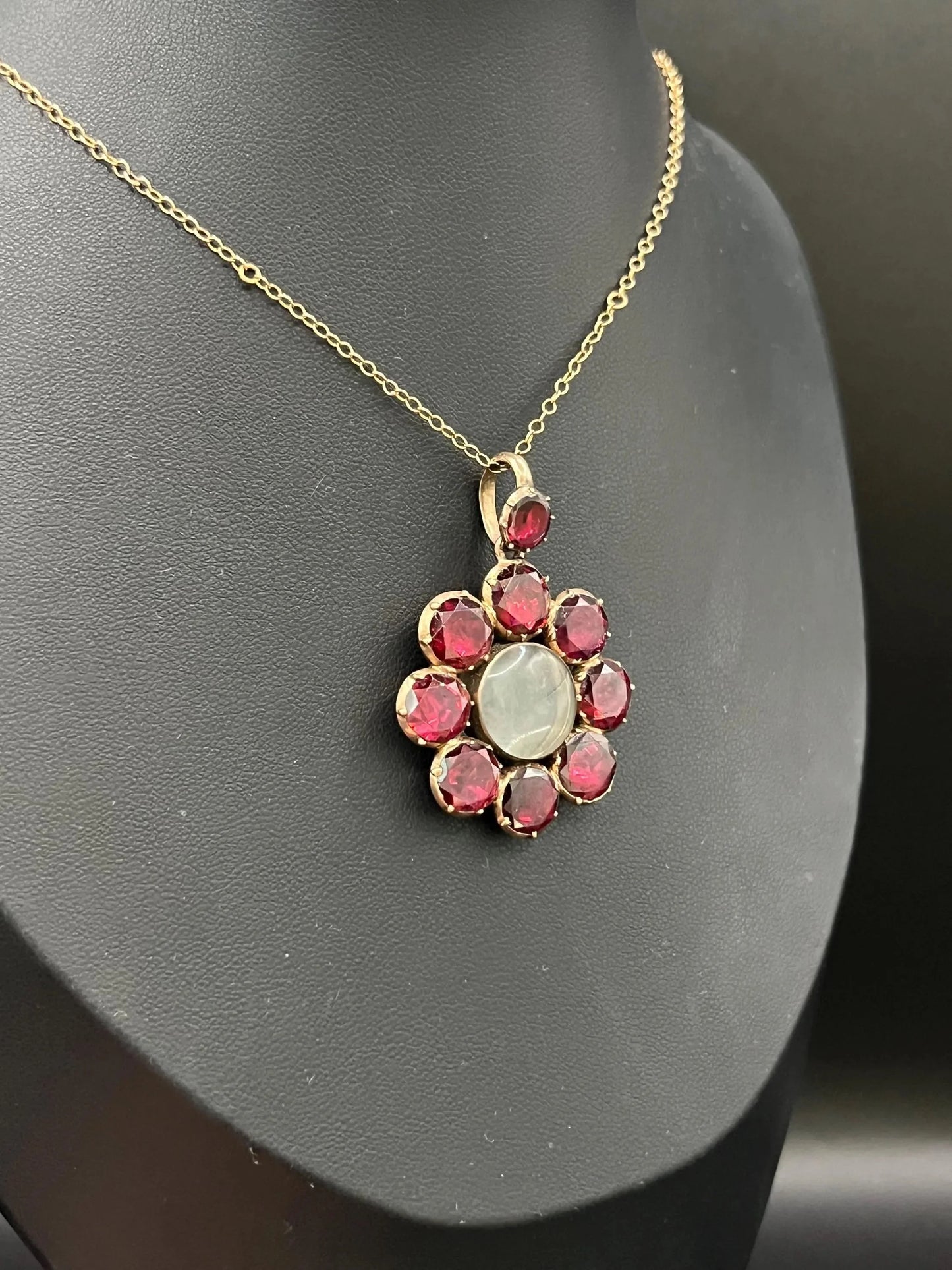 An antique garnet locket pendant in gold, with a chain, on a black bust