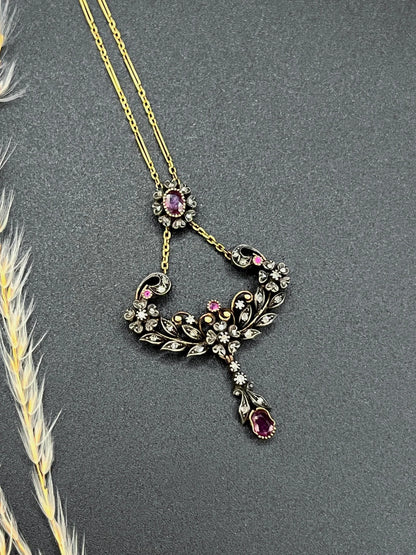 An ornate pendant with rubies and diamonds in gold and silver, with an integrated chain, on a black background
