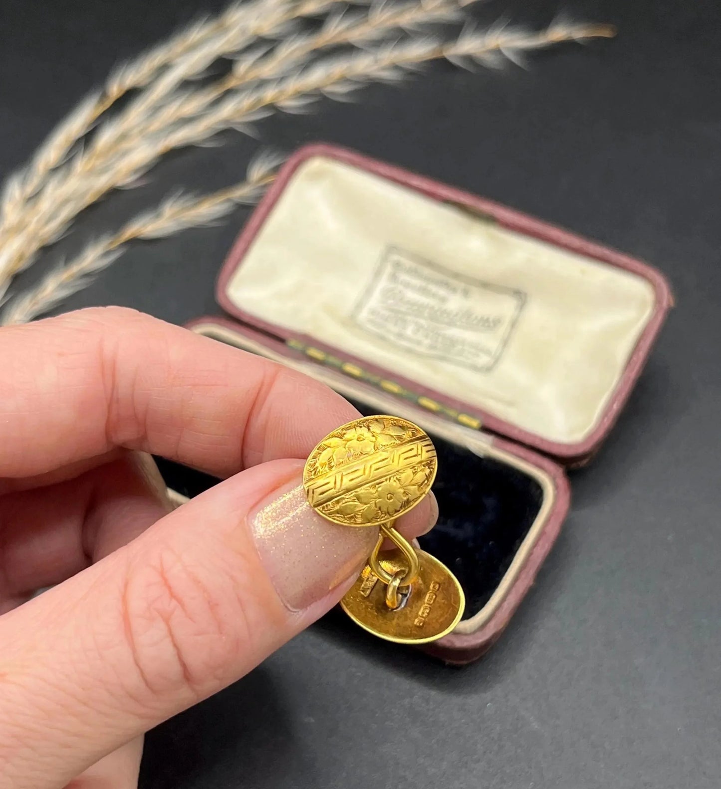 A pair of oval yellow gold floral engraved cufflinks, held in a hand