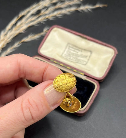 A pair of oval yellow gold floral engraved cufflinks, held in a hand