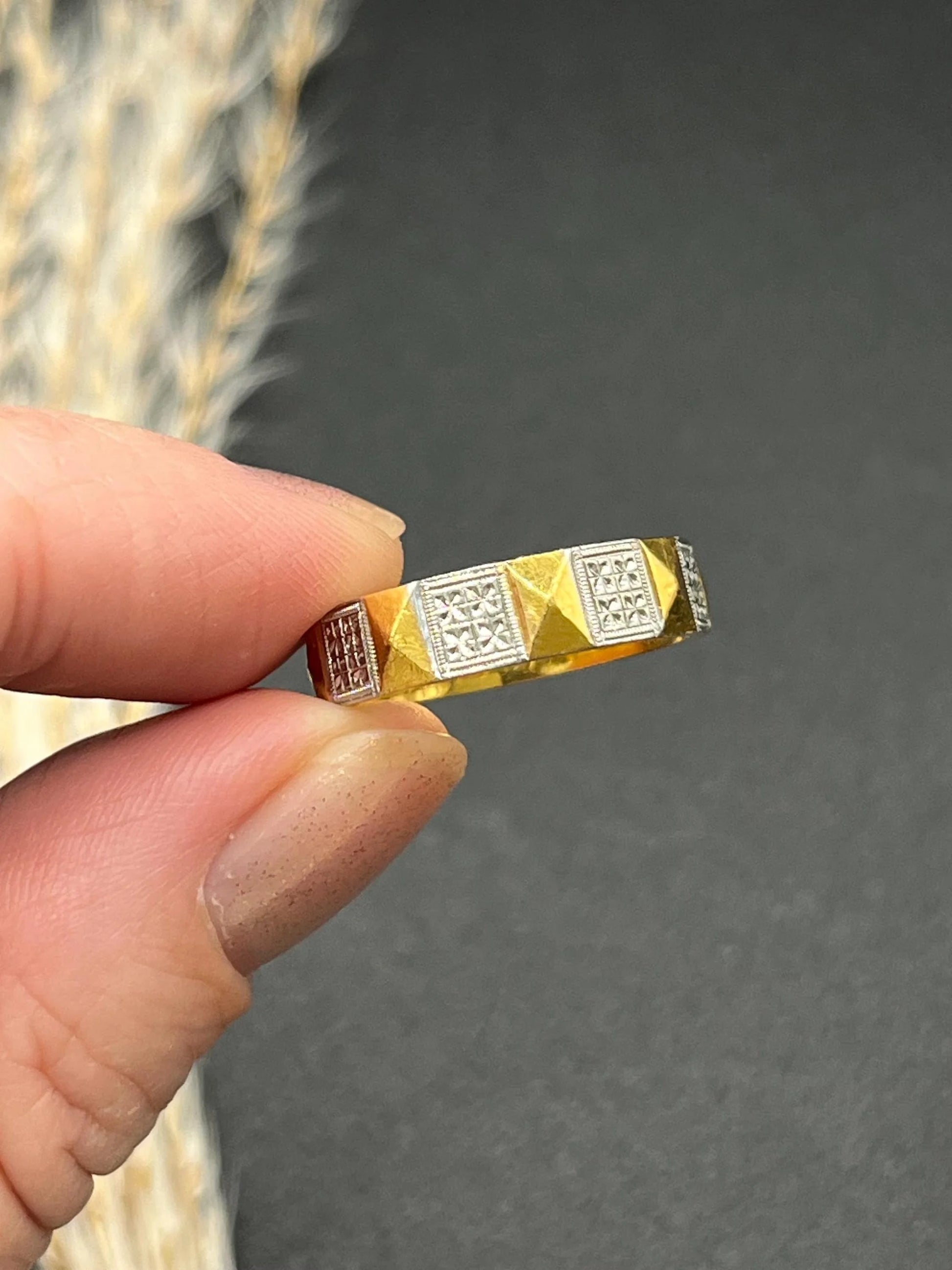 A yellow gold and platinum geometric band ring, held in a hand