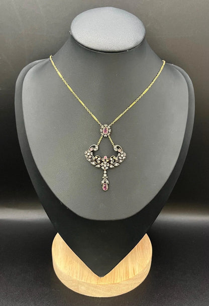 An ornate pendant with rubies and diamonds in gold and silver, with an integrated chain, modelled on a black jewellery bust