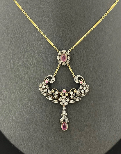 An ornate pendant with rubies and diamonds in gold and silver, with an integrated chain, on a black background