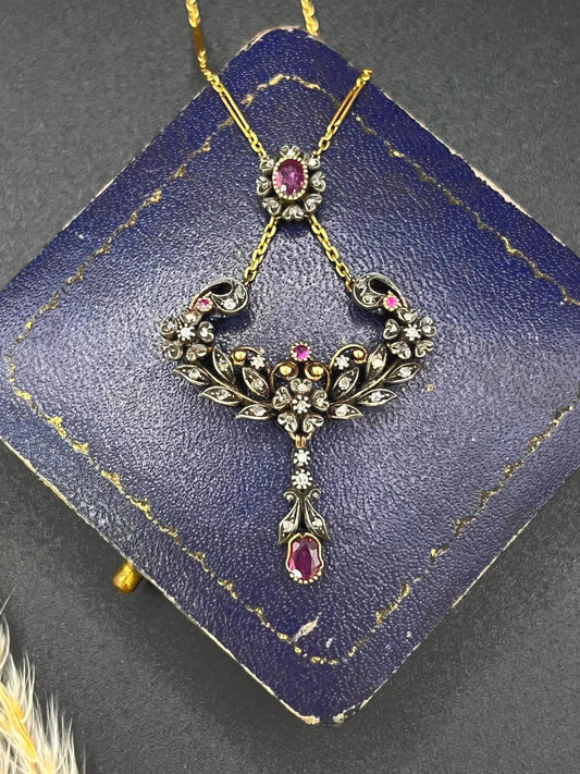 An ornate pendant with rubies and diamonds in gold and silver, with an integrated chain, on an antique box