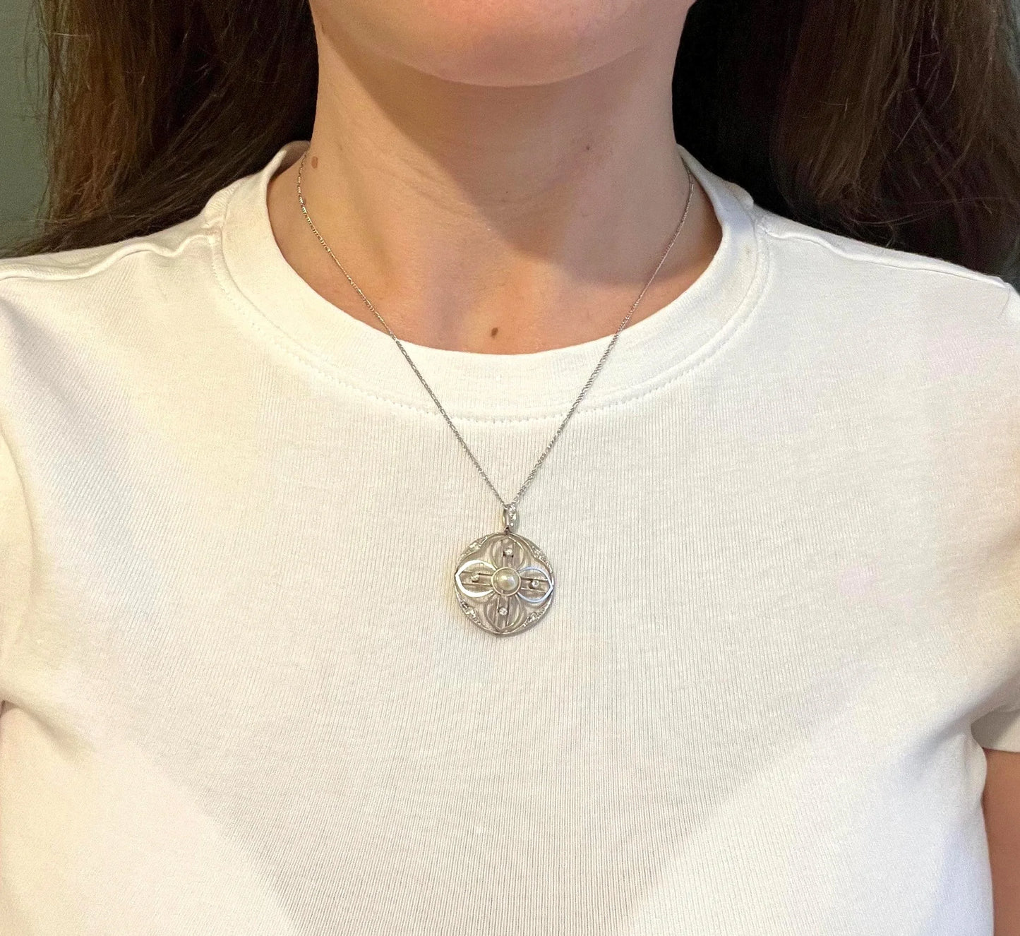 A circular openwork pendant with a pearl and diamonds, in yellow gold and platinum, with a chain, modelled by a woman