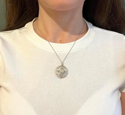 A circular openwork pendant with a pearl and diamonds, in yellow gold and platinum, with a chain, modelled by a woman