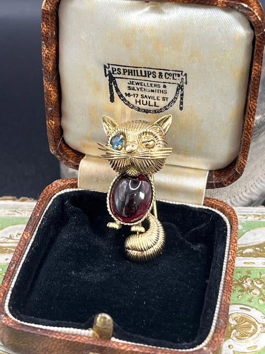 A yellow gold stylised cat brooch with garnet body and sapphire eye