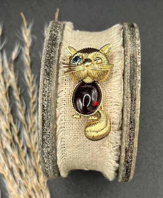 A yellow gold stylised cat brooch with garnet body and sapphire eye