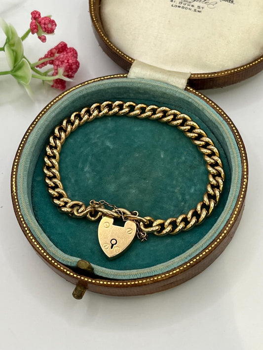 A gold curb link bracelet with a heart shaped padlock clasp, in an antique box