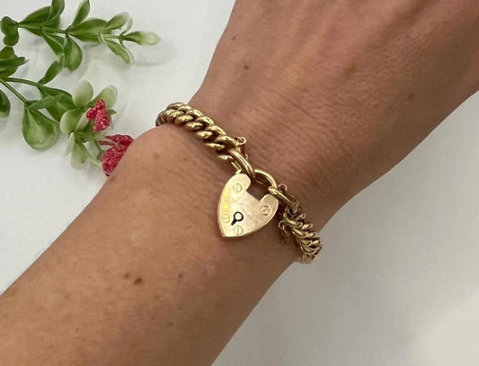 A gold curb link bracelet with a heart shaped padlock clasp, modelled on a wrist