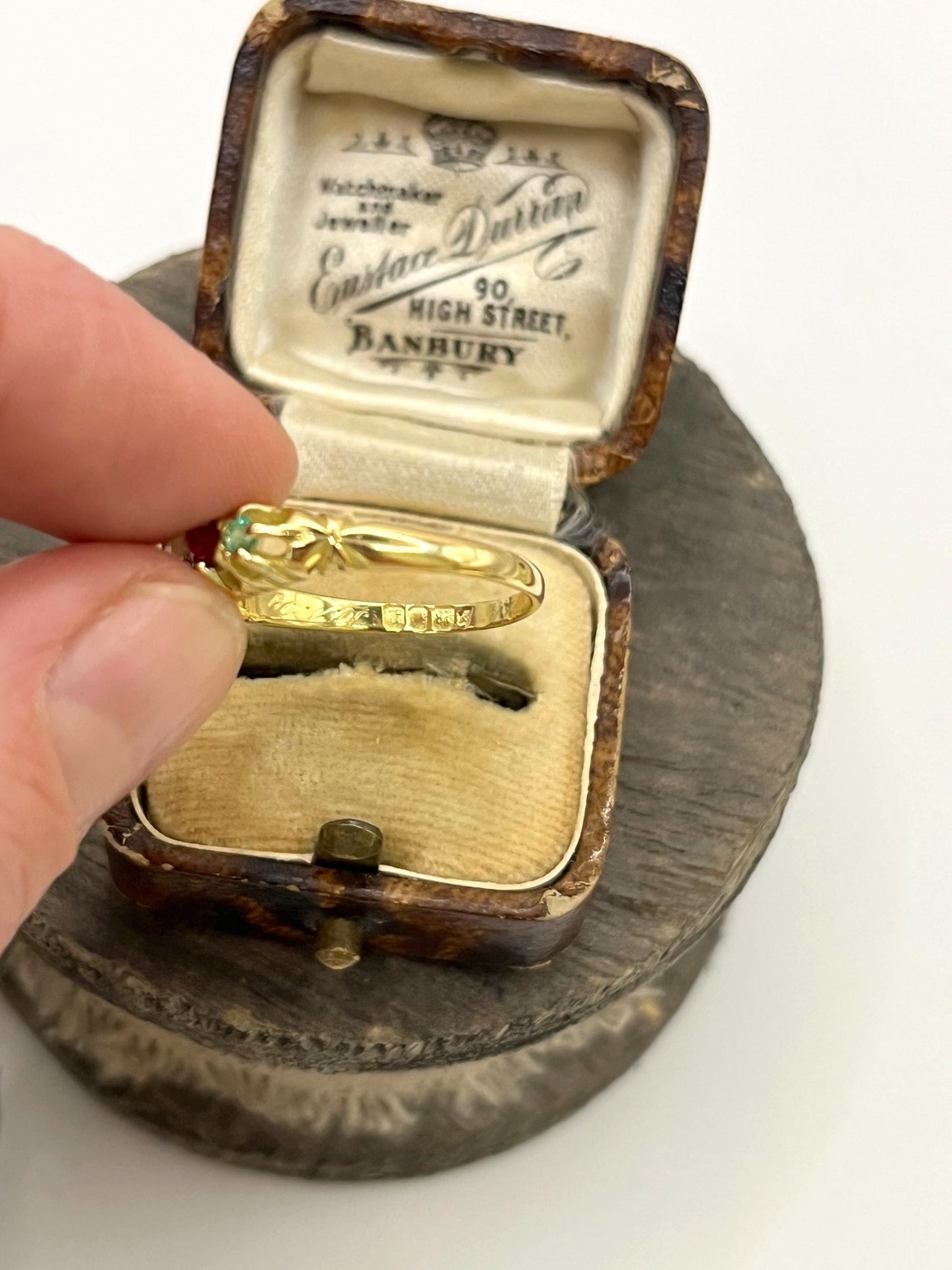 A yellow gold five stone acrostic multi-gemstone ring, held in a hand