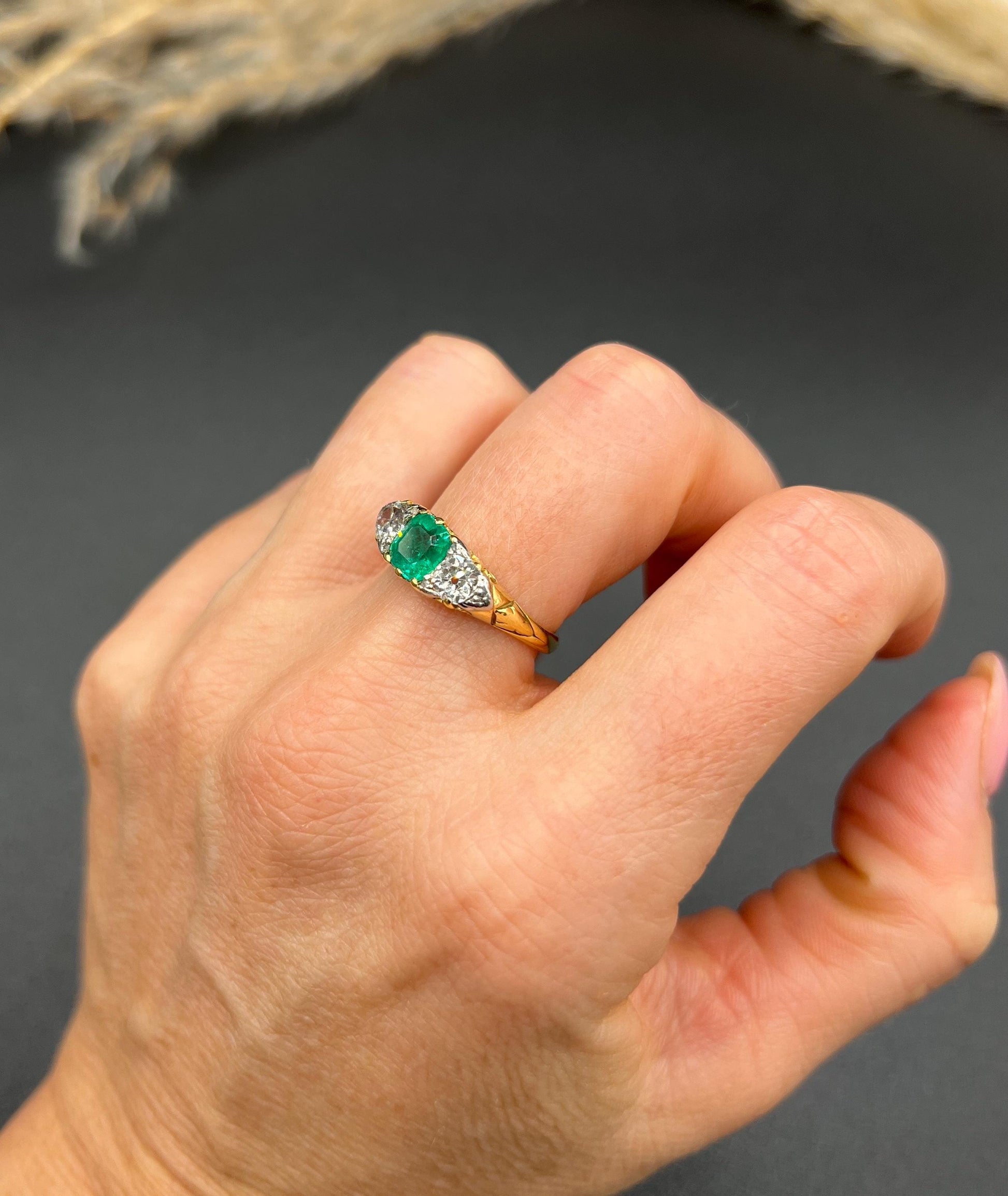 A three stone old cut emerald and diamond ring in yellow gold, modelled on a hand