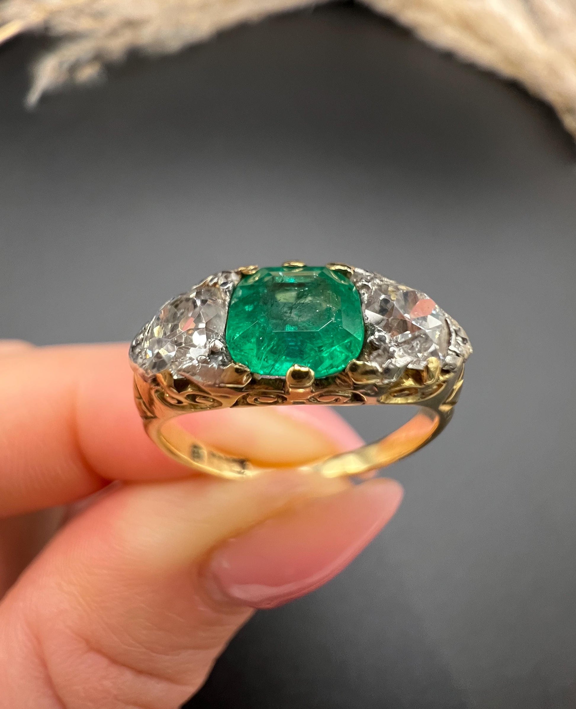 A three stone old cut emerald and diamond ring in yellow gold, held in a hand