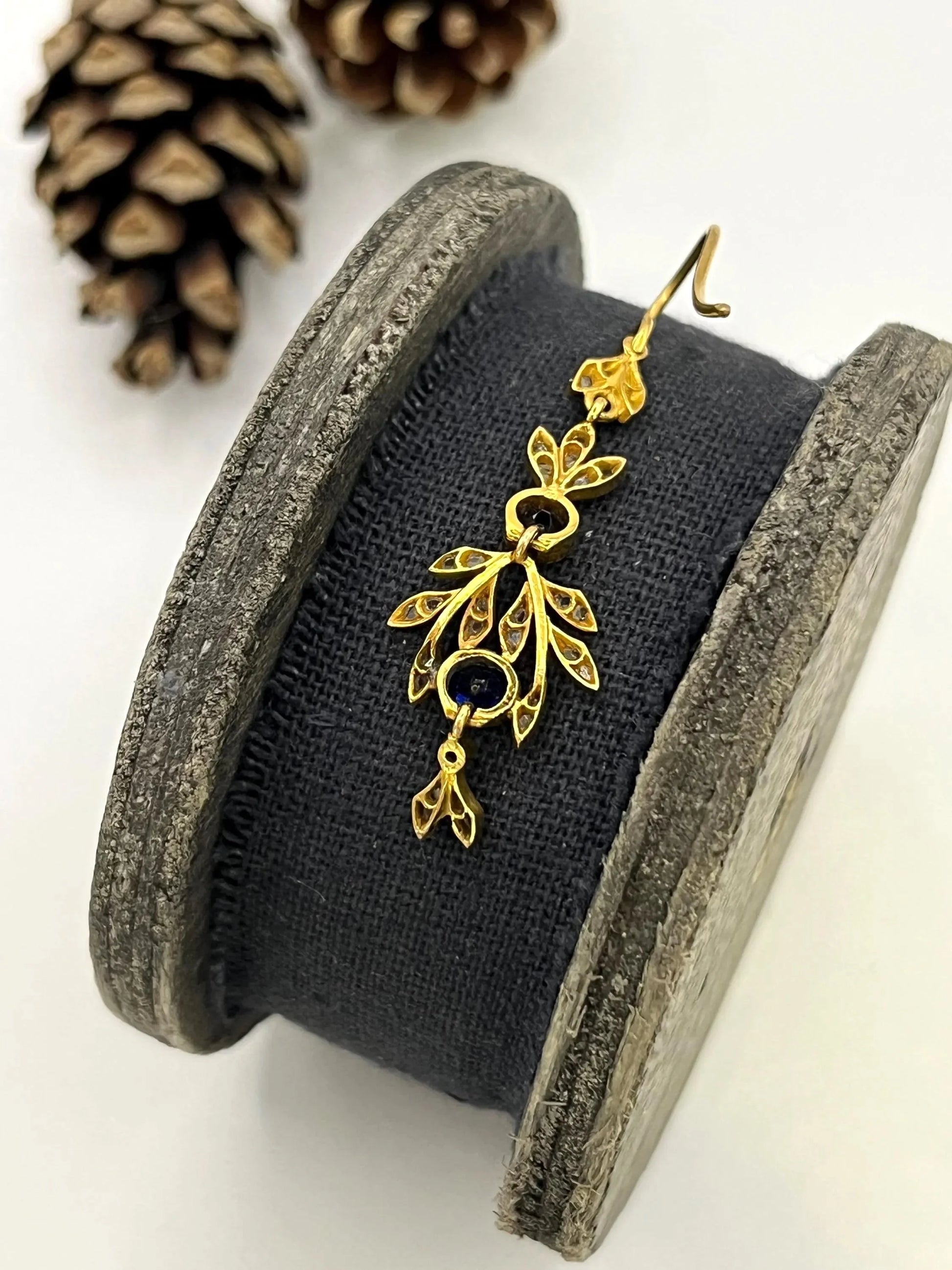 A sapphire and diamond foliate drop earring in yellow gold, on a wooden spool