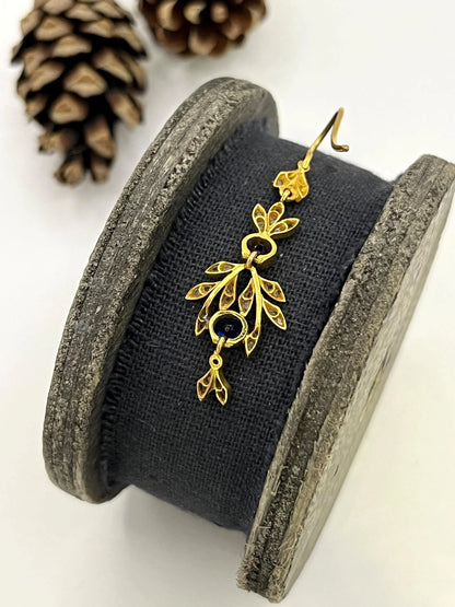 A sapphire and diamond foliate drop earring in yellow gold, on a wooden spool