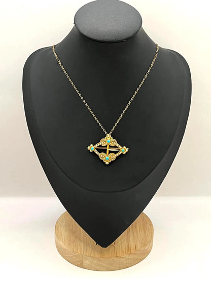 A yellow gold buckle style brooch/pendant with turquoise and seed pearls, with a chain, on a black jewellery bust