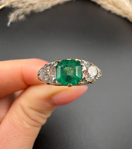 A three stone old cut emerald and diamond ring in yellow gold, held in a hand