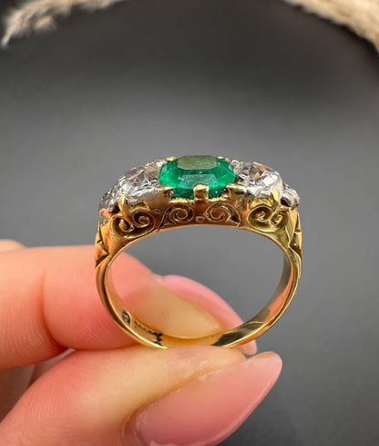 A three stone old cut emerald and diamond ring in yellow gold, held in a hand