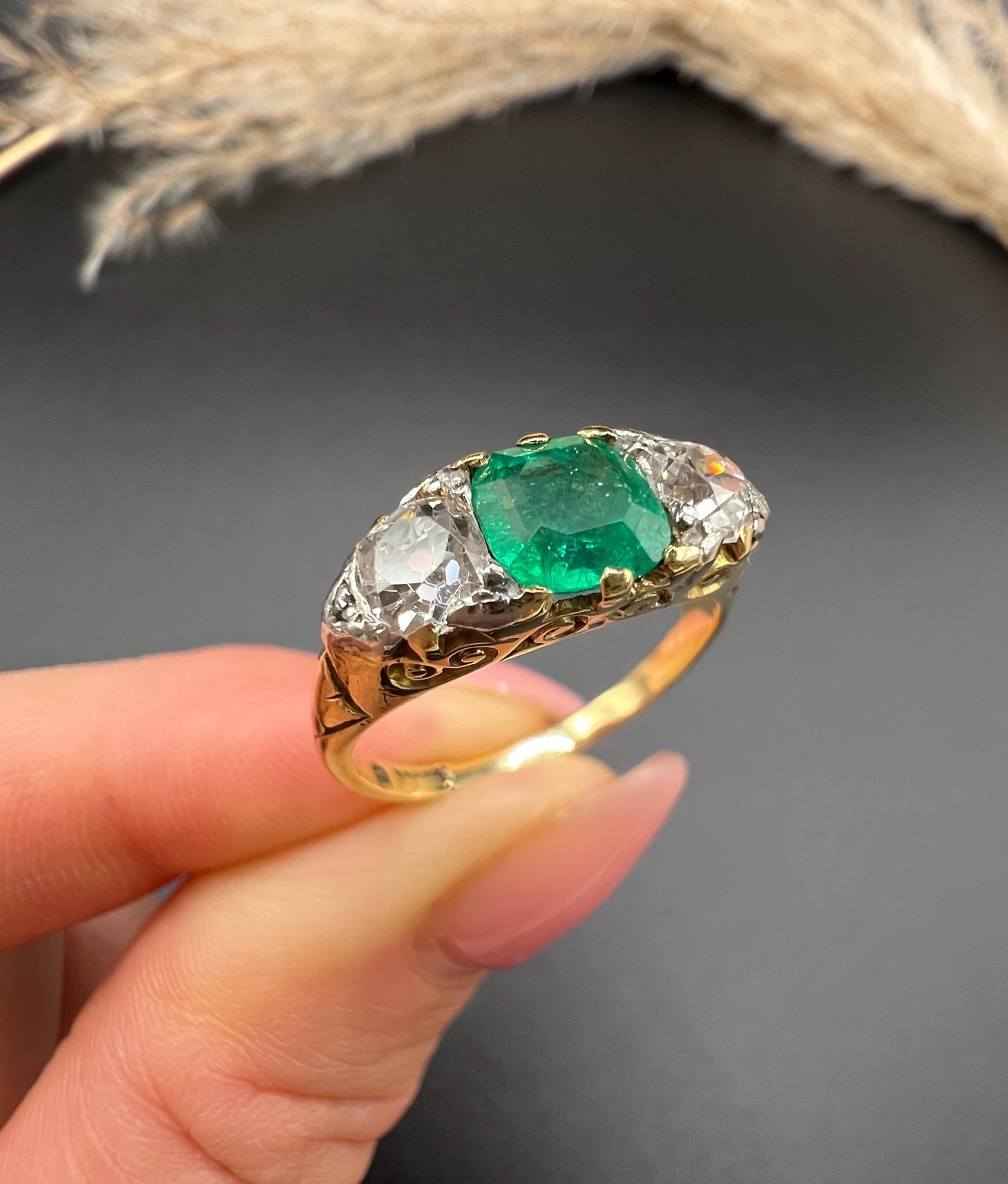 A three stone old cut emerald and diamond ring in yellow gold, held in a hand
