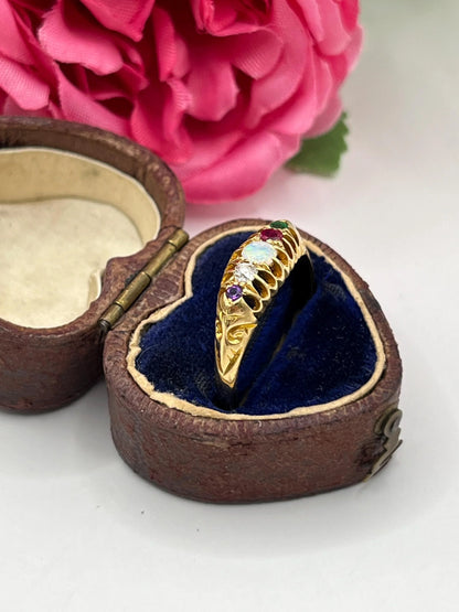 A five stone acrostic ADORE ring in yellow gold, in a heart-shaped ring box