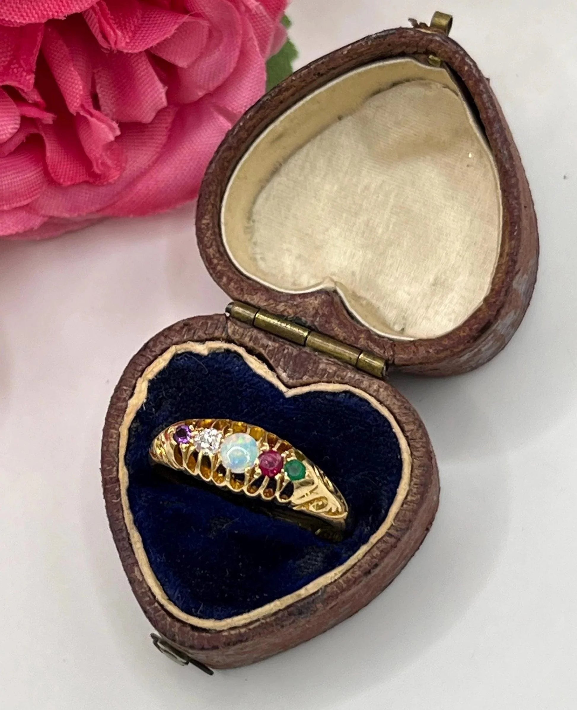 A five stone acrostic ADORE ring in yellow gold, in a heart-shaped ring box