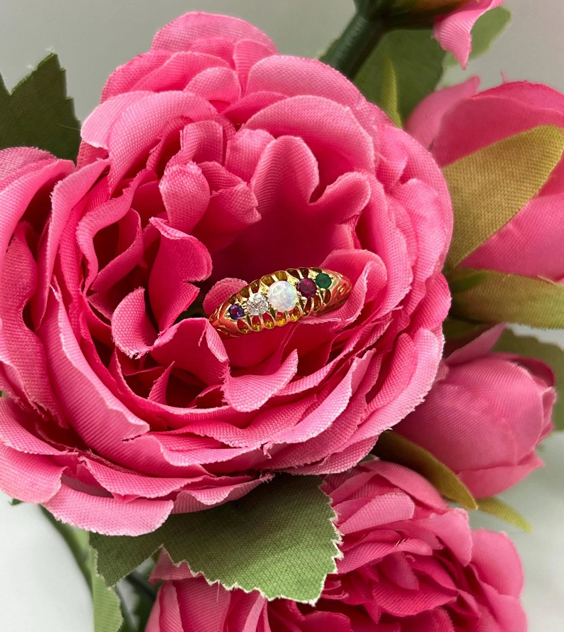 A five stone acrostic ADORE ring in yellow gold, in a pink flower