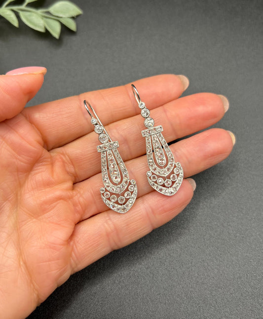 A pair of antique platinum diamond drop earrings, held in a hand
