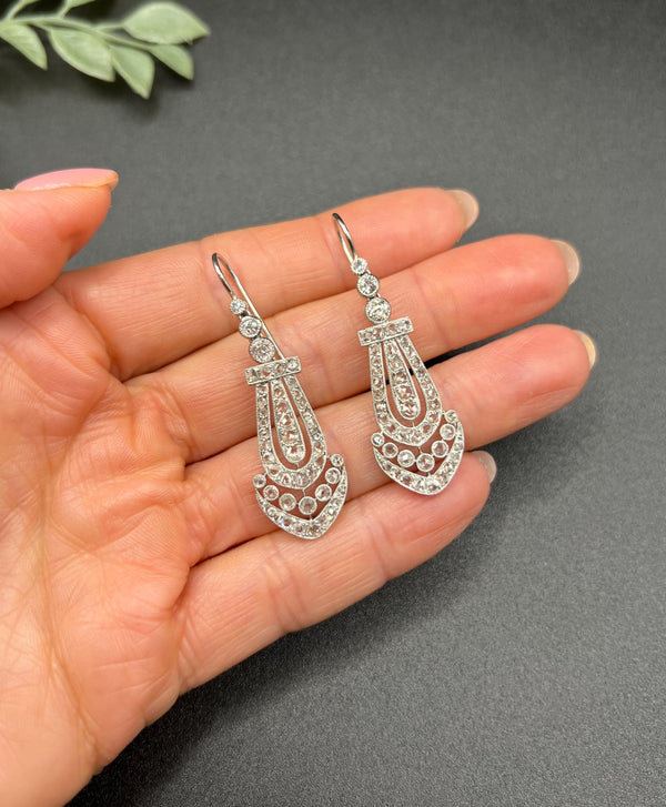 A pair of antique platinum diamond drop earrings, held in a hand