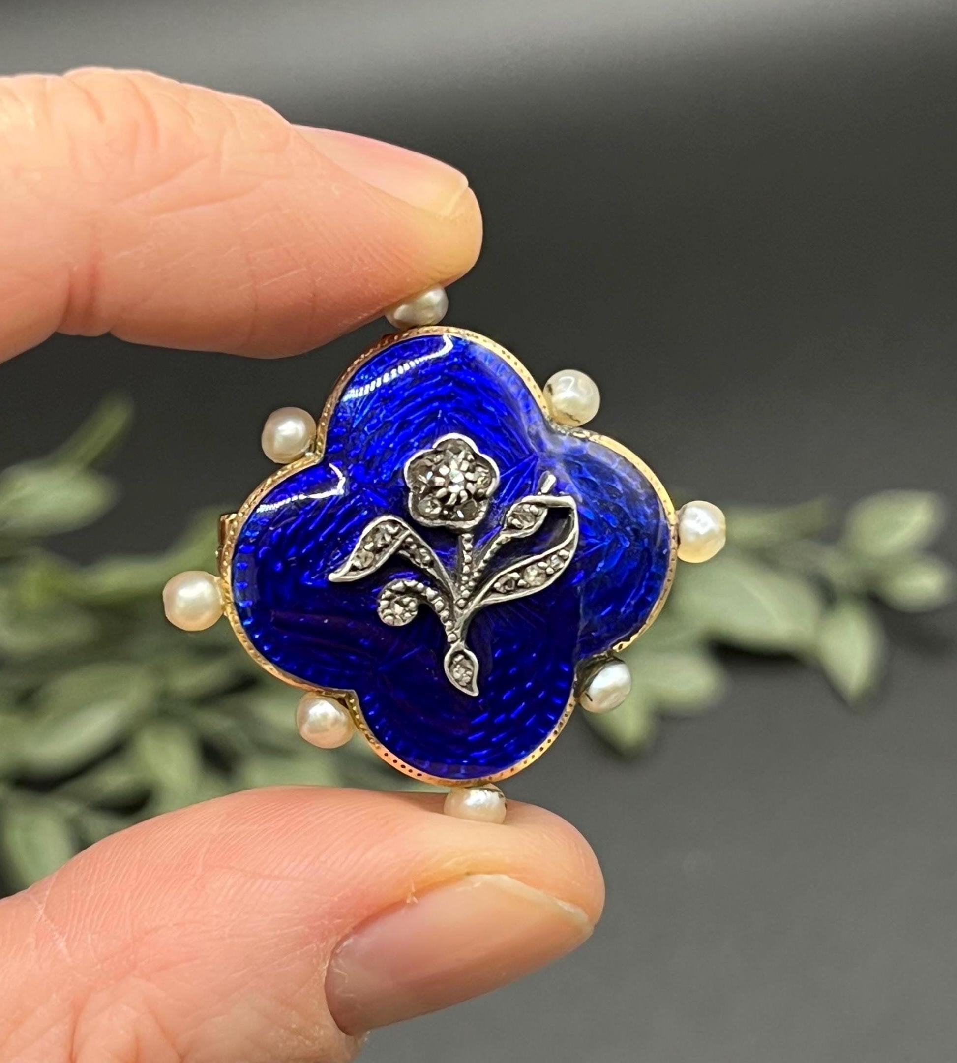 A diamond flower, blue enamel and pearl brooch in yellow gold, held in a hand