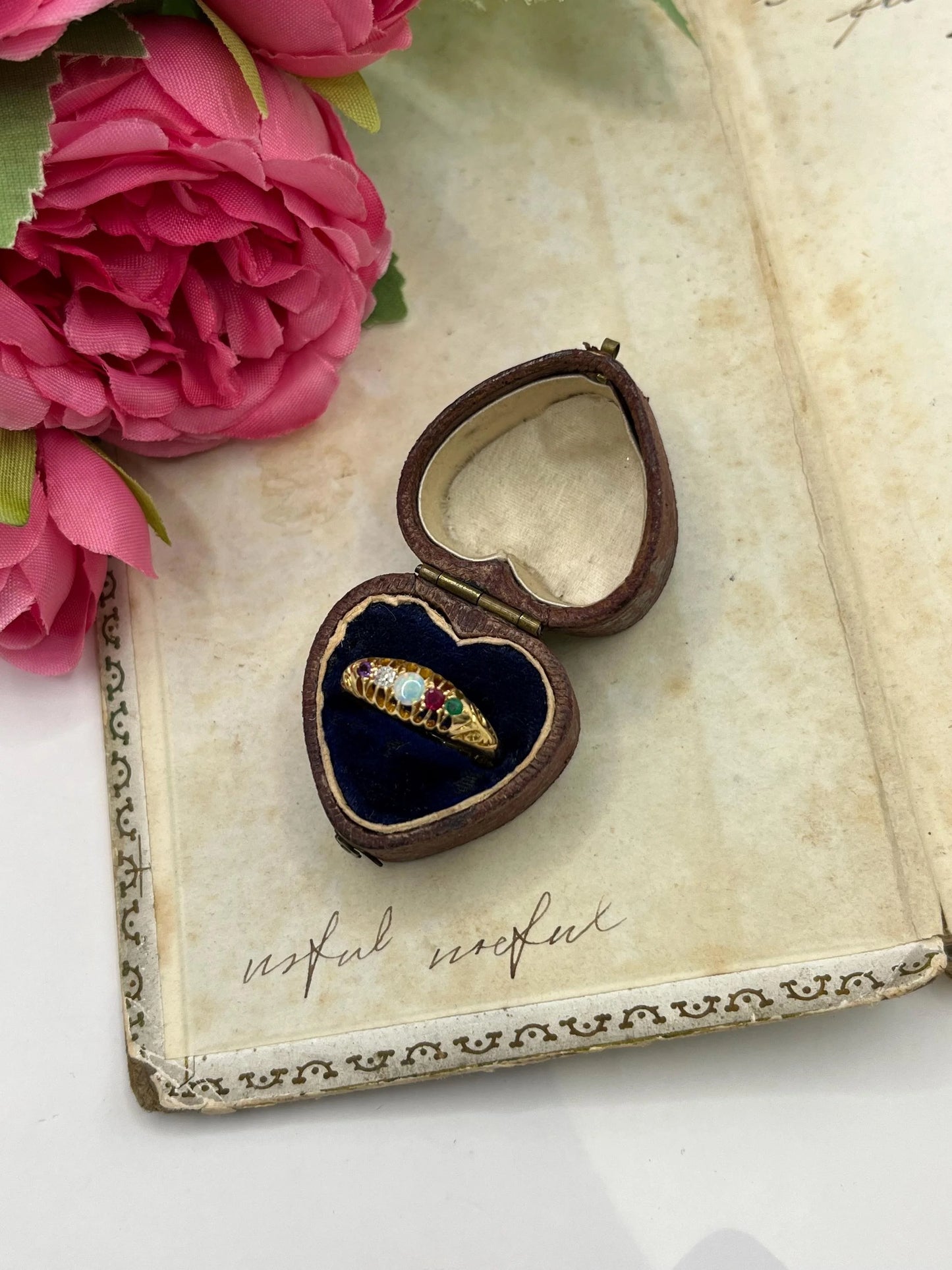 A five stone acrostic ADORE ring in yellow gold, in a heart-shaped ring box