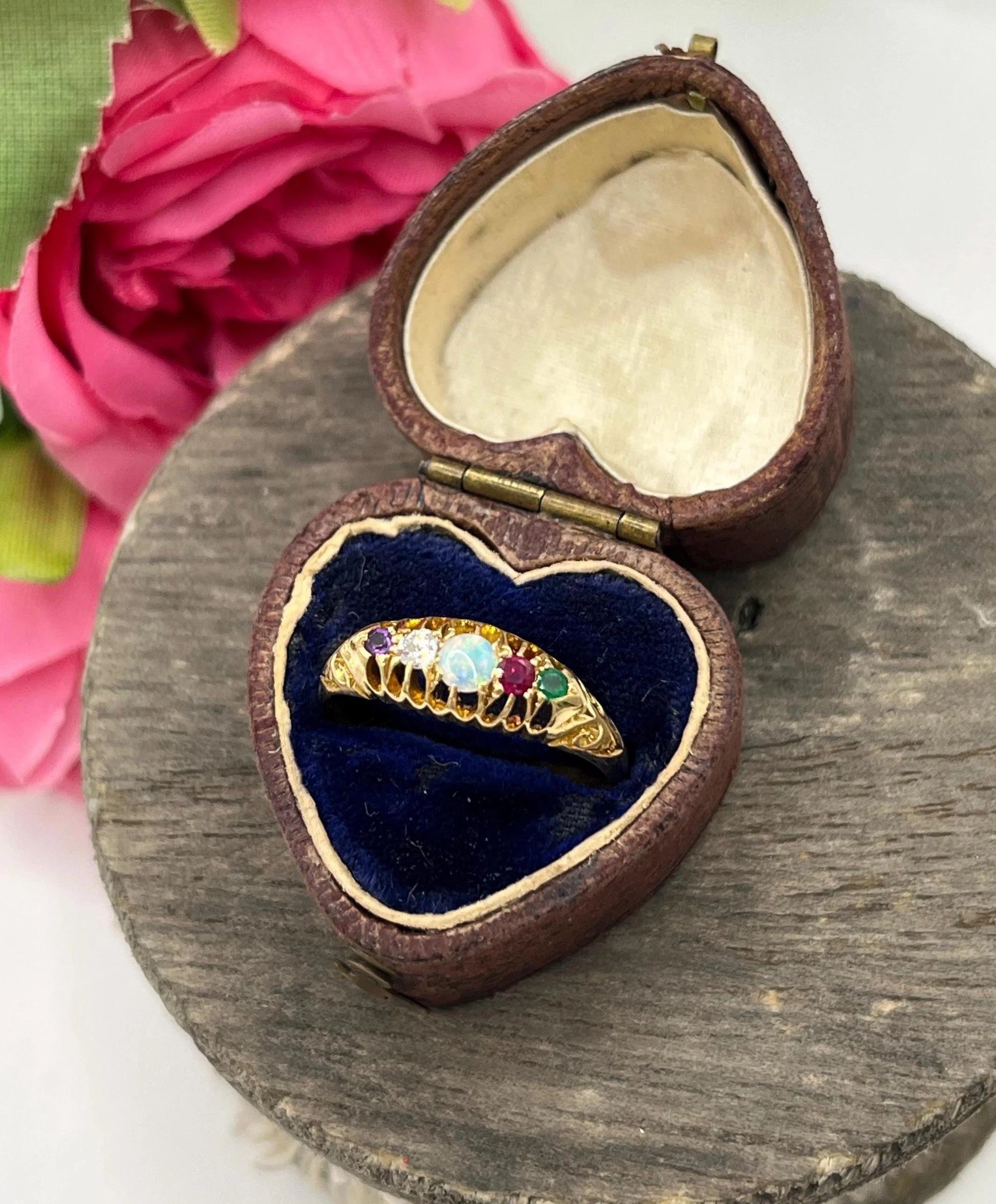 A five stone acrostic ADORE ring in yellow gold, in a heart-shaped ring box