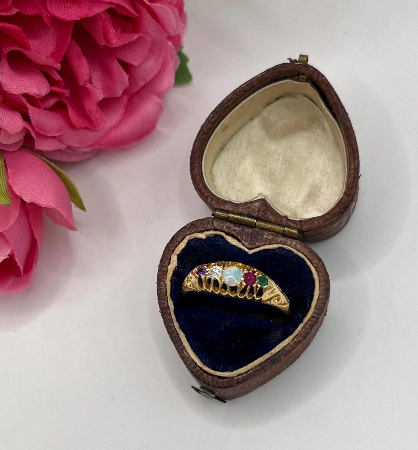 A five stone acrostic ADORE ring in yellow gold, in a heart-shaped ring box