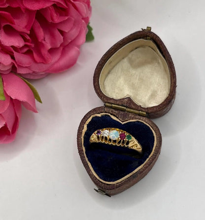 A five stone acrostic ADORE ring in yellow gold, in a heart-shaped ring box