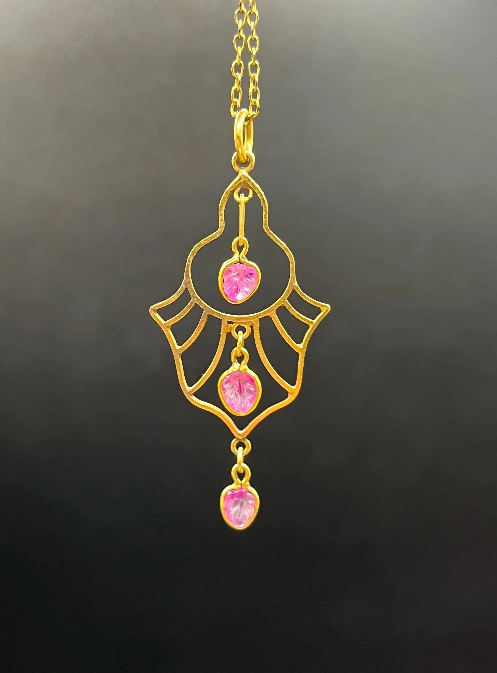 A yellow gold three stone ruby openwork drop pendant on a yellow gold chain