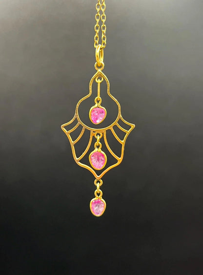 A yellow gold three stone ruby openwork drop pendant on a yellow gold chain