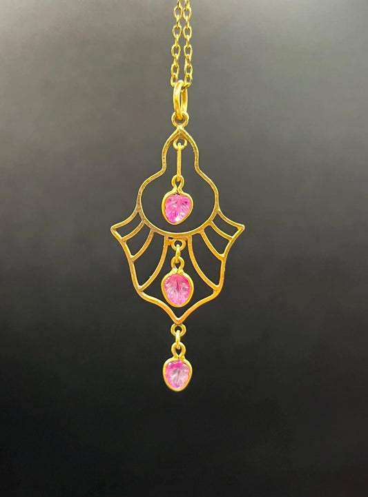 A yellow gold three stone ruby openwork drop pendant on a yellow gold chain