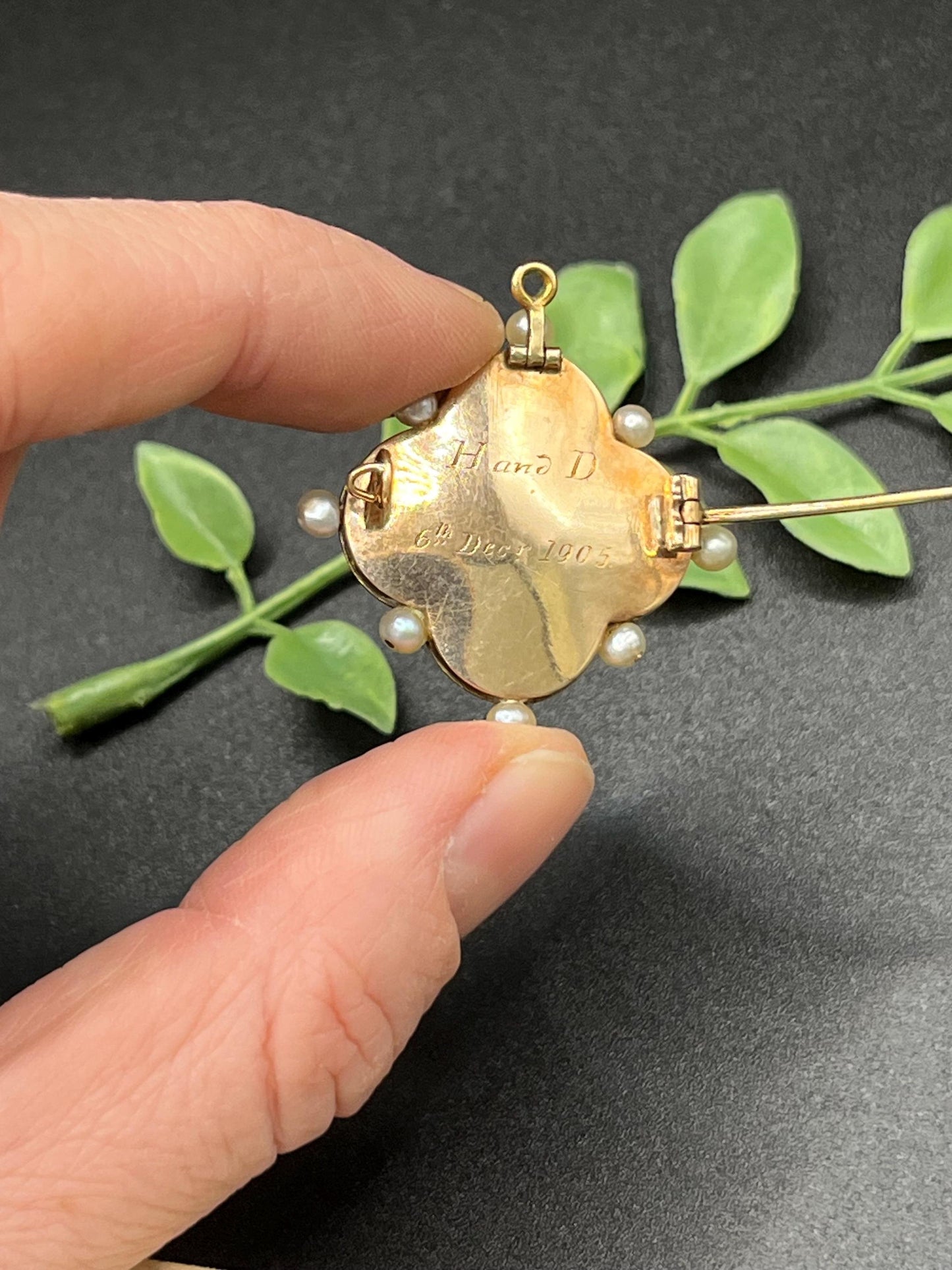 A diamond flower, blue enamel and pearl brooch in yellow gold, engraved on the back, held in a hand
