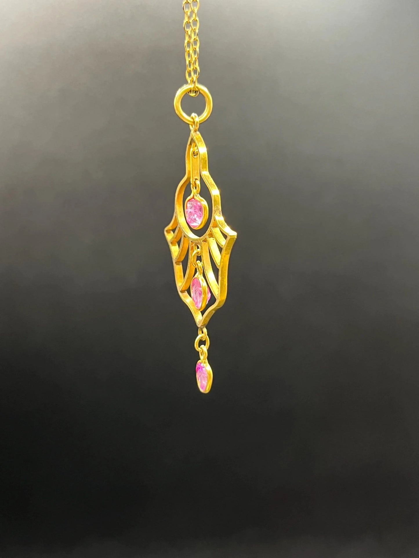 A yellow gold three stone ruby openwork drop pendant on a yellow gold chain