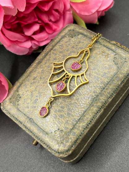 A yellow gold three stone ruby openwork drop pendant on a yellow gold chain