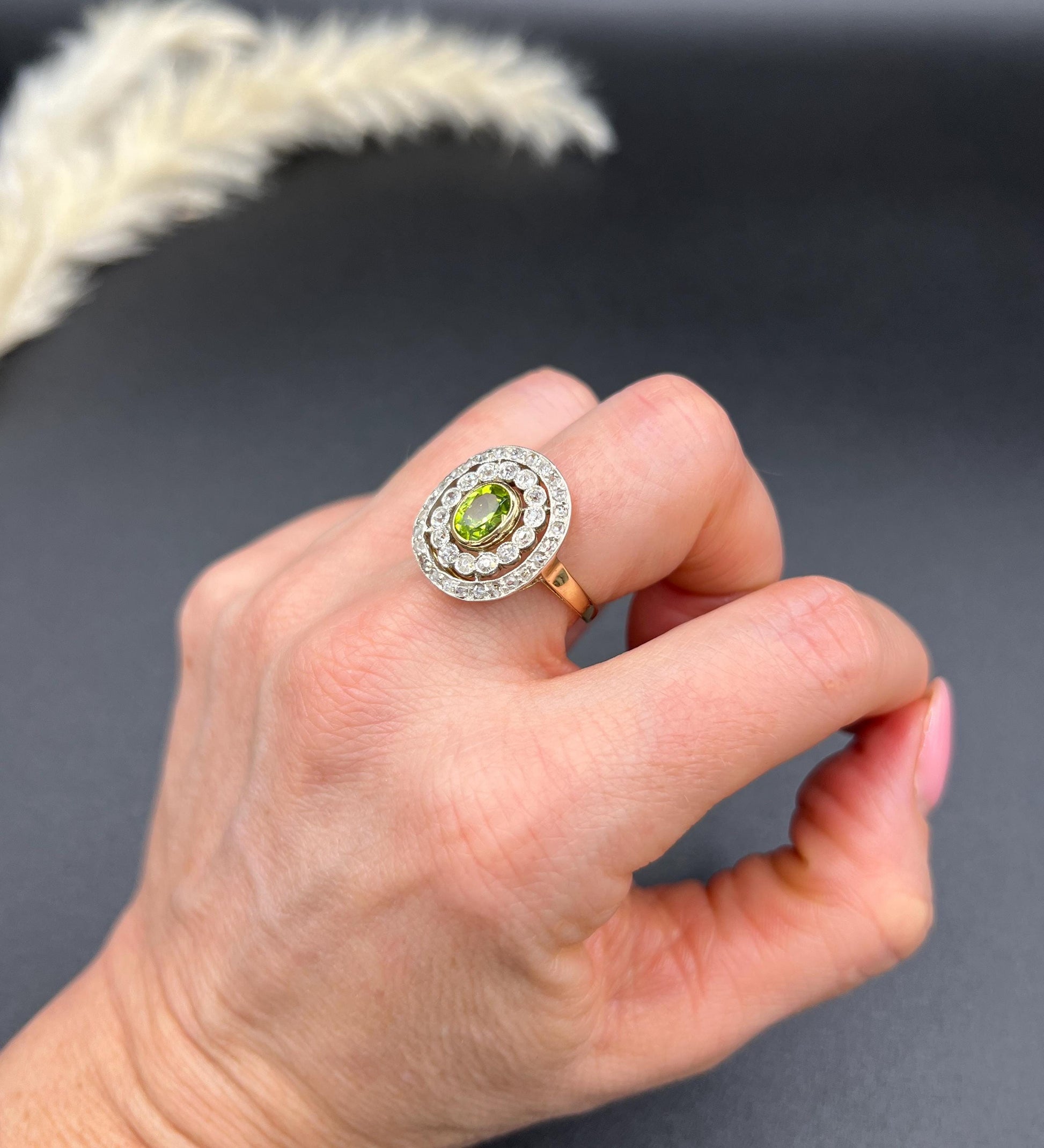 An oval peridot and old cut diamond fancy cluster ring in yellow gold and platinum, modelled on a hand