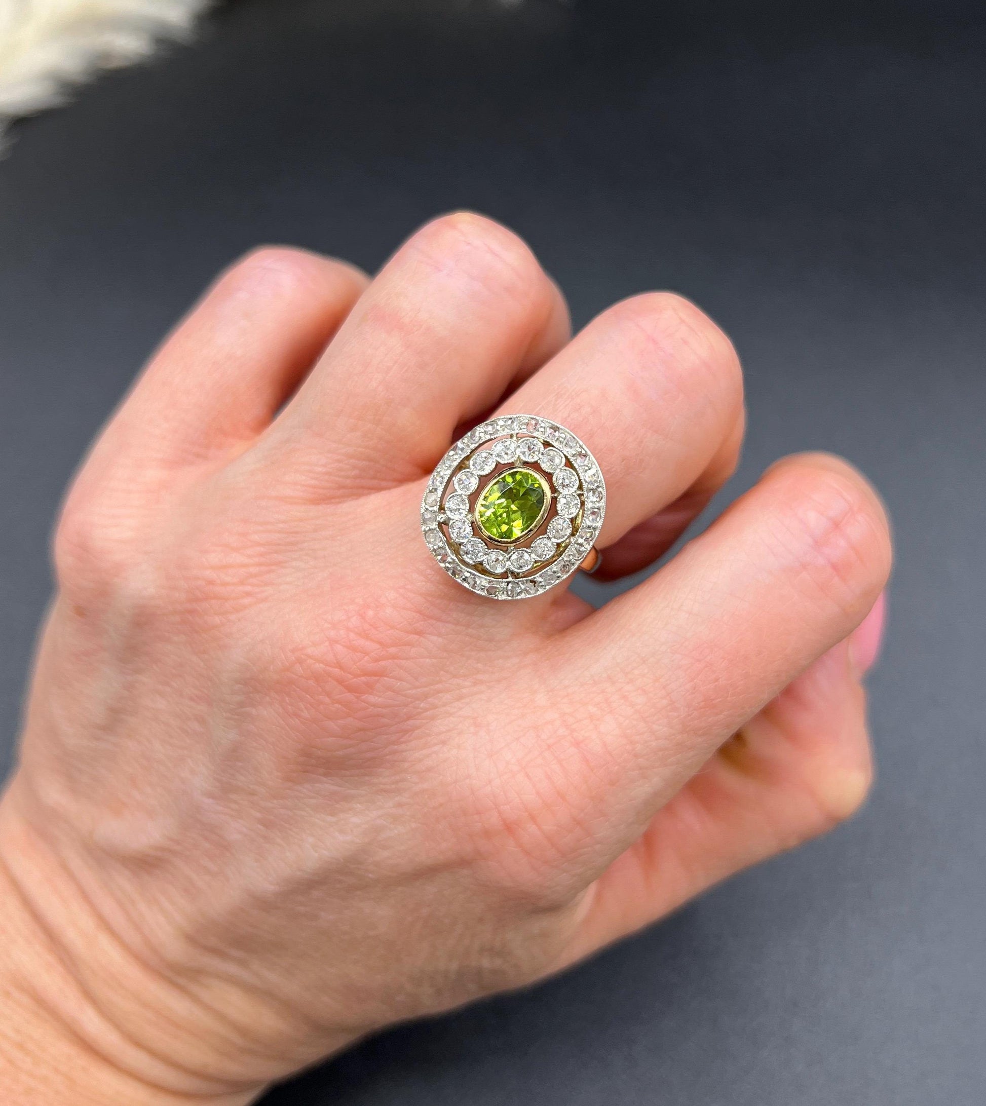 An oval peridot and old cut diamond fancy cluster ring in yellow gold and platinum, modelled on a hand