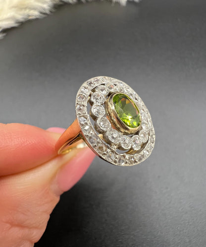 An oval peridot and old cut diamond fancy cluster ring in yellow gold and platinum held in a hand