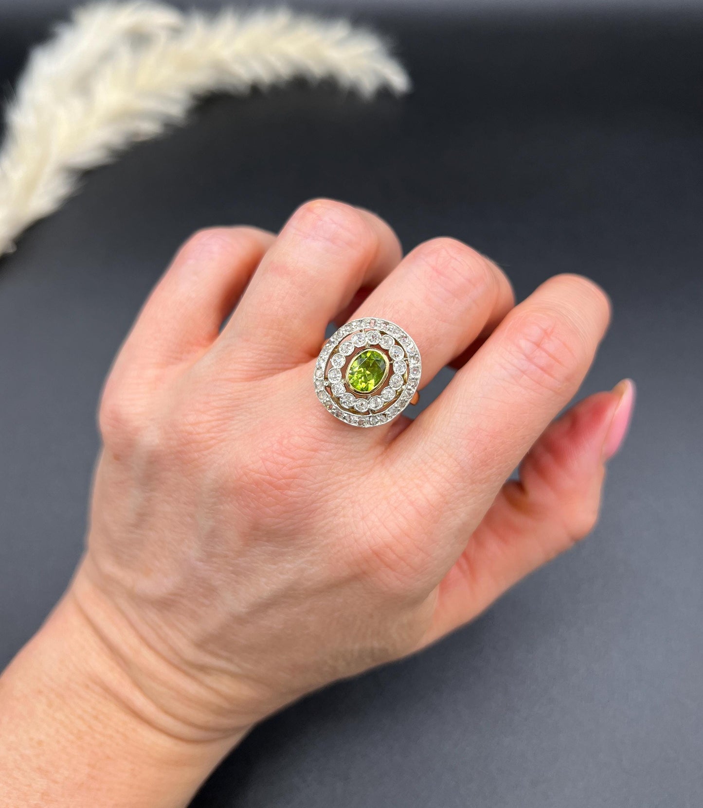 An oval peridot and old cut diamond fancy cluster ring in yellow gold and platinum, modelled on a hand