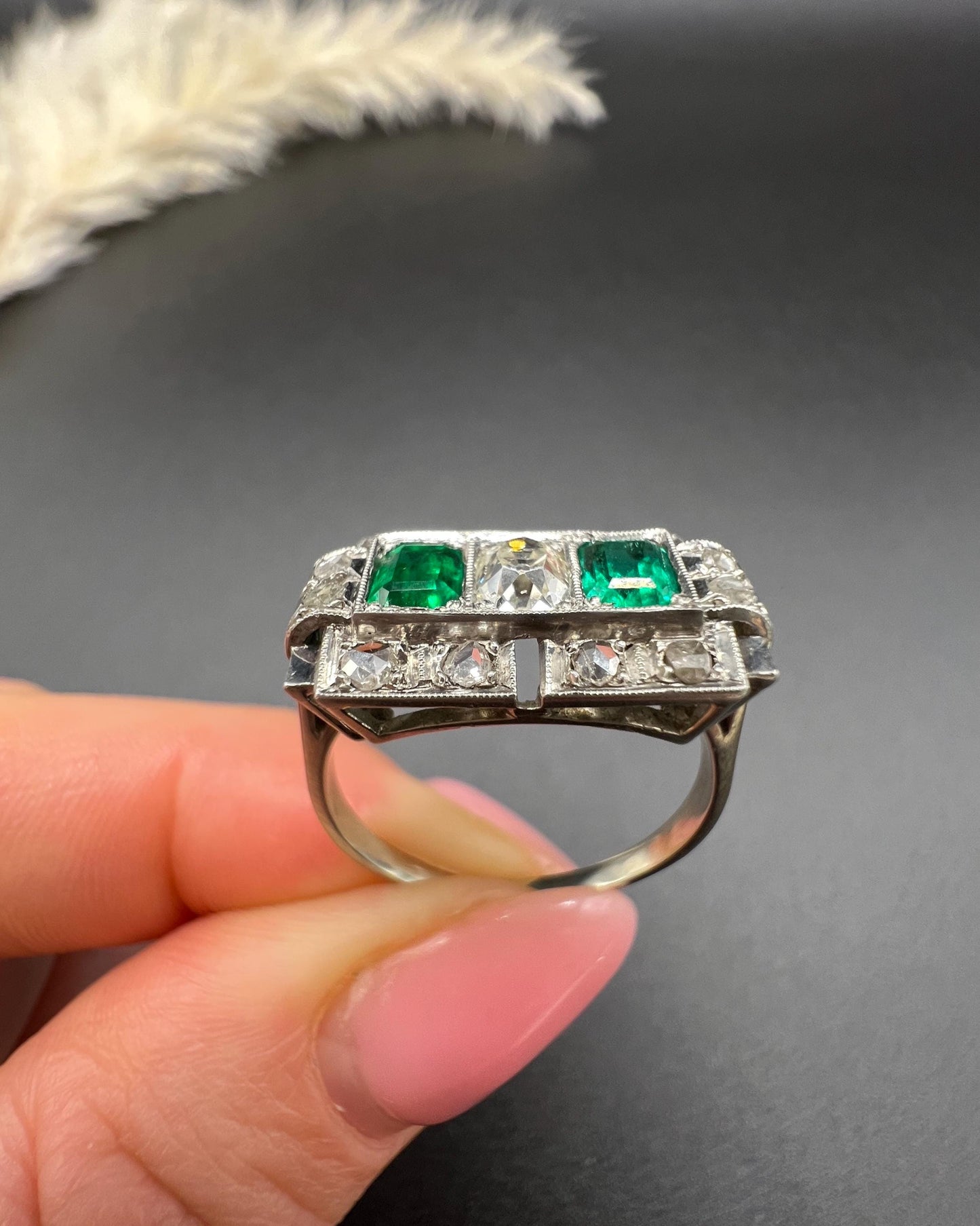 An emerald and old cut diamond rectangular ring in platinum, held in a hand