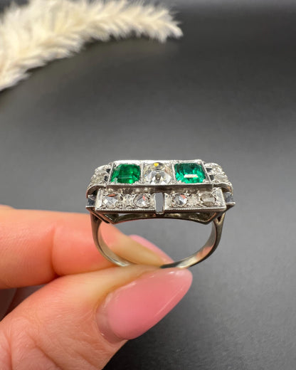 An emerald and old cut diamond rectangular ring in platinum, held in a hand