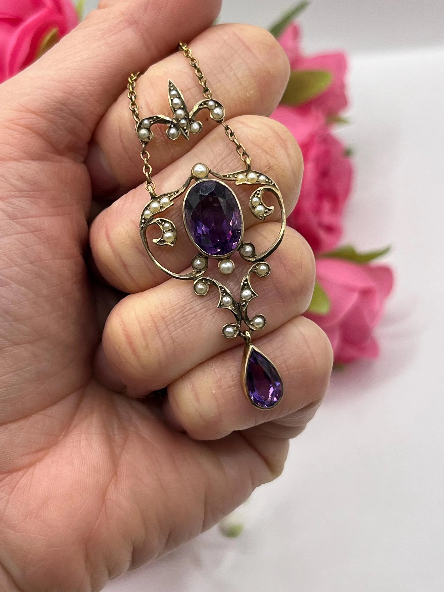 An amethyst and seed pearl pendant necklace in yellow gold, held in a hand