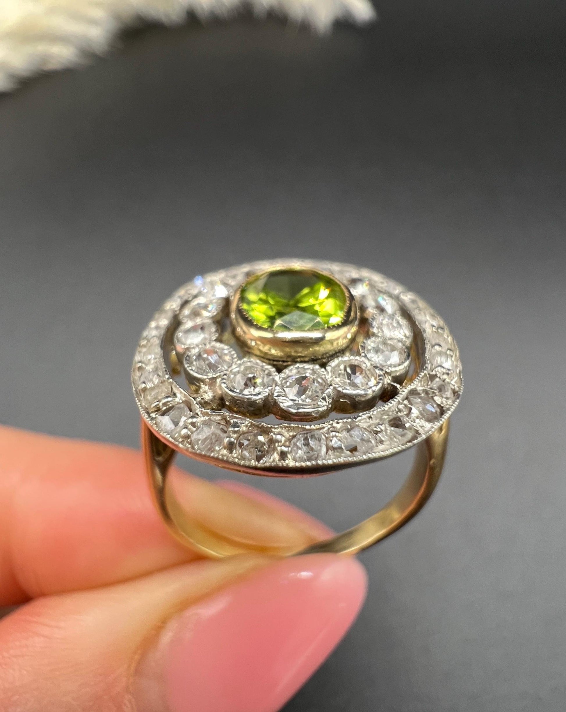An oval peridot and old cut diamond fancy cluster ring in yellow gold and platinum, held in a hand